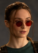 Sophie Turner as Lara Croft wears round sunglasses with red lenses in the series Tomb Raider.